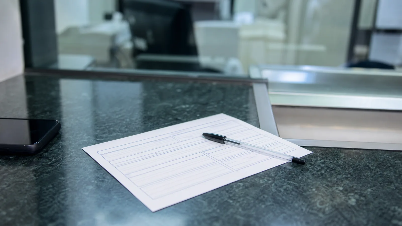Blank bank transfer form and pen on a bank counter beside a smartphone